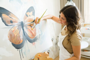 Female inspired woman artist using a brush and painting a butterfly