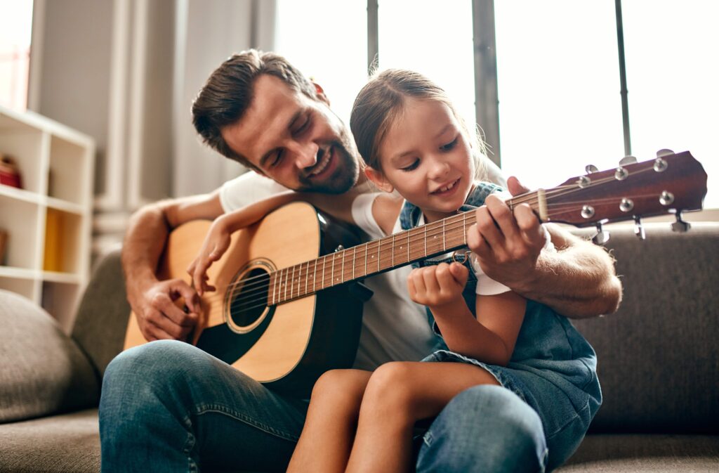 Happy dad teaches his cute daughter to play the guitar