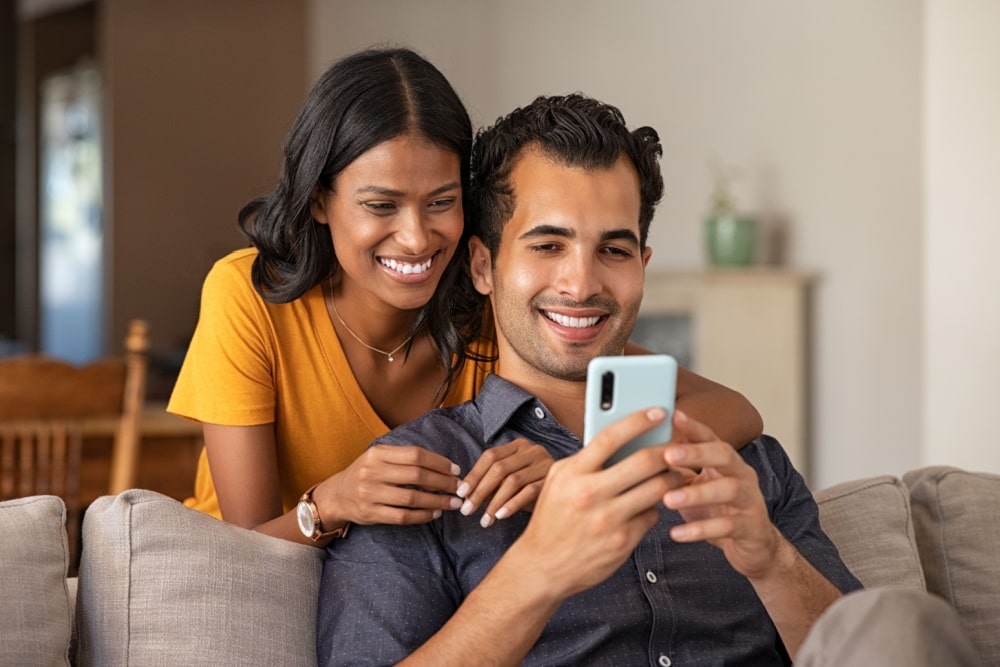 Couple using smartphone together at home. Man sitting on couch