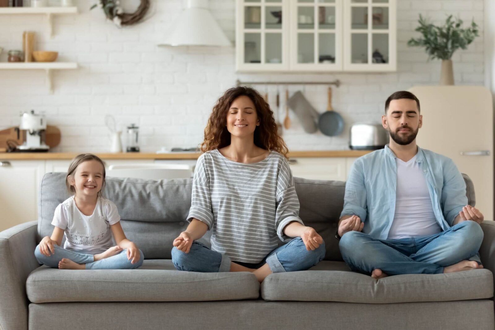 Calm young family with little daughter sit on couch practice yoga together