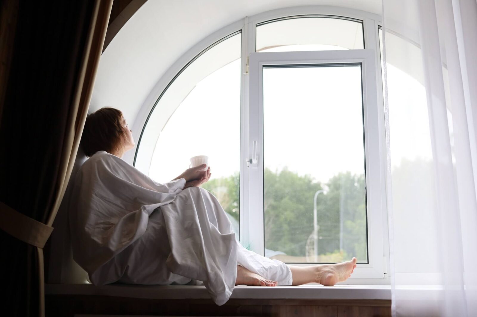 A woman drinking coffee in the window's background