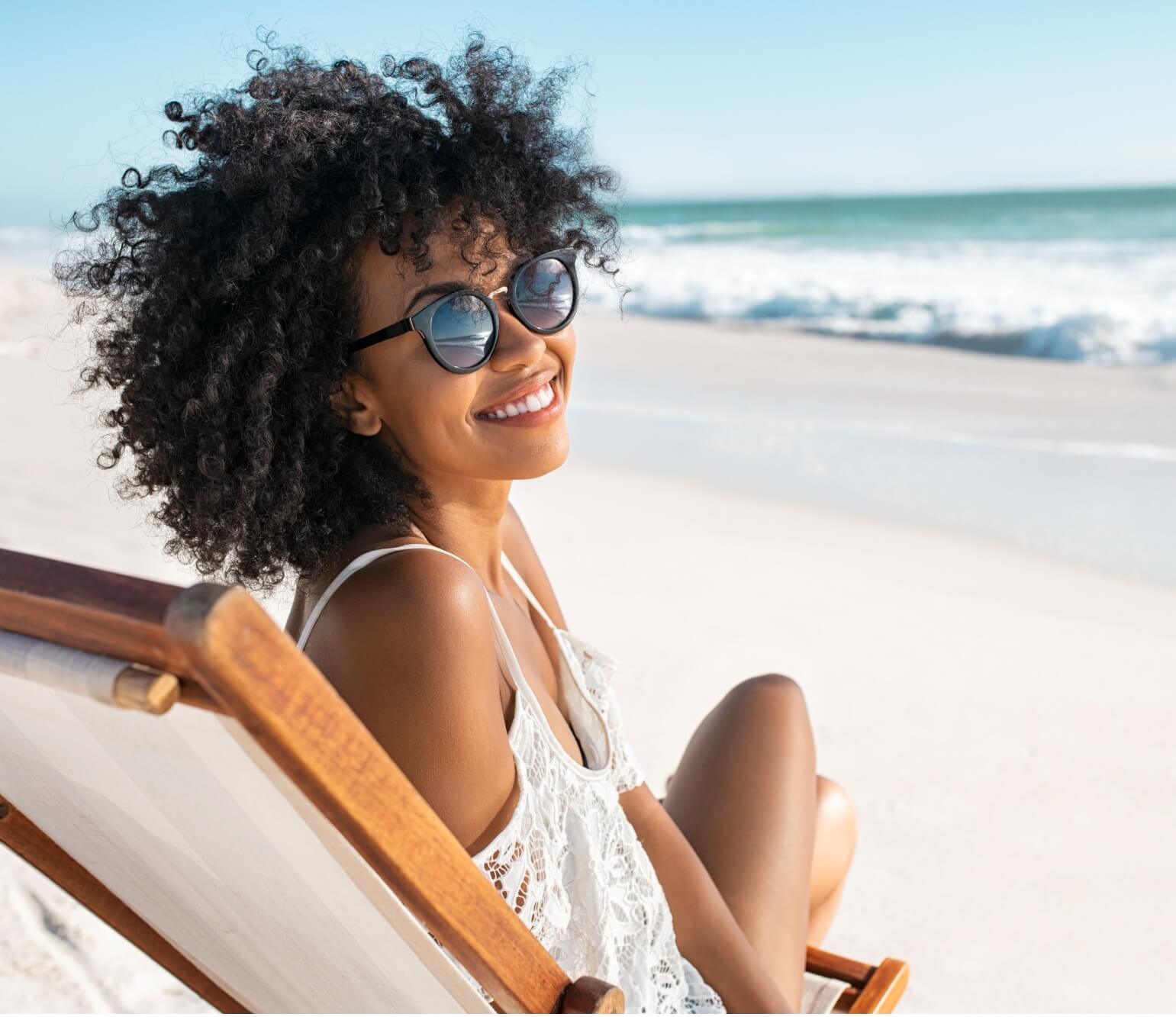 happy young black woman relaxing on chair at tropical beach